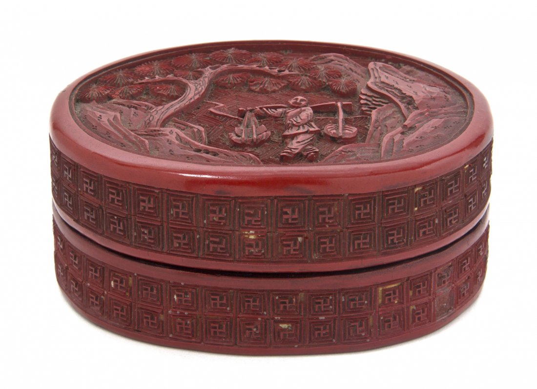 A Chinese Cinnabar Lacquered Box, Width 3 7/8 inches.: A Chinese Cinnabar Lacquered Box, of oval form, depicting a figure carrying items under a pine tree. Width 3 7/8 inches.