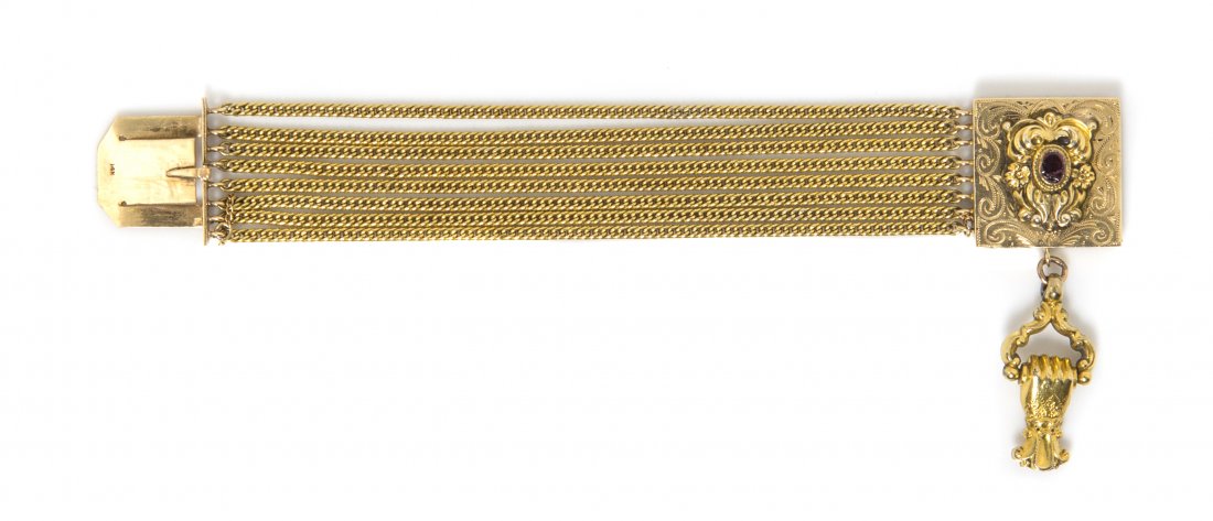 A 14 Karat Yellow Gold and Garnet Multi Strand Bracelet: A 14 Karat Yellow Gold and Garnet Multi Strand Bracelet, consisting of eight curb link chains joined with an engraved box clasp surmounted with a scroll and foliate motif gold plaque containing one ov