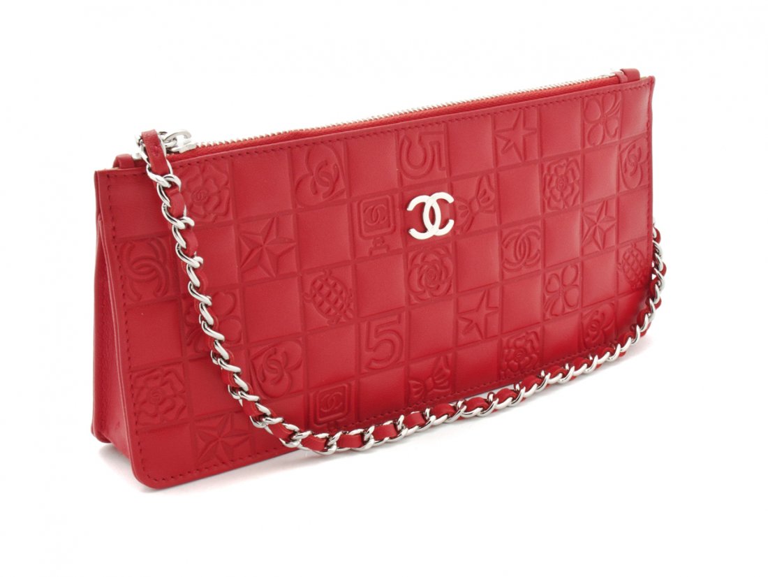 A Chanel Red Embossed Leather Clutch, 8 1/2 x 4 x 1 inc: A Chanel Red Embossed Leather Clutch, embossed with number fives, camellia flowers, clovers, stars, logos, and perfume bottles in a checkerboard pattern, silvertone and red leather chainlink shoulder 
