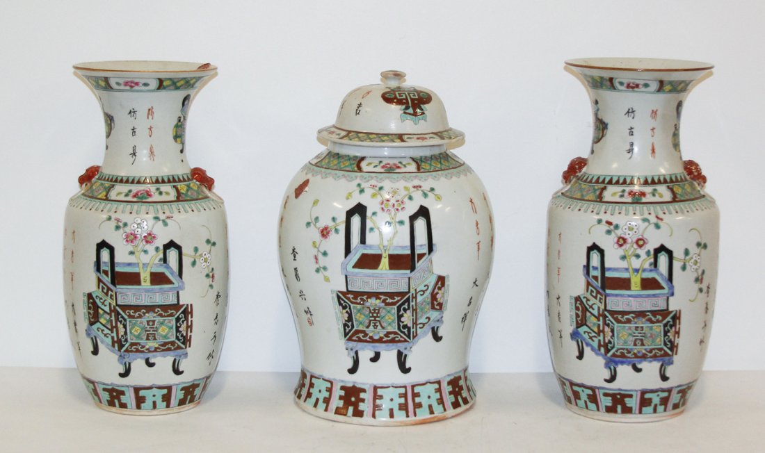 A Chinese Three-Piece Porcelain Garniture, Height of ta: A Chinese Three-Piece Porcelain Garniture, comprising a covered squat baluster form urn, and a pair of handled baluster vases, each having polychrome decoration, depicting archaic vessels, and with ca