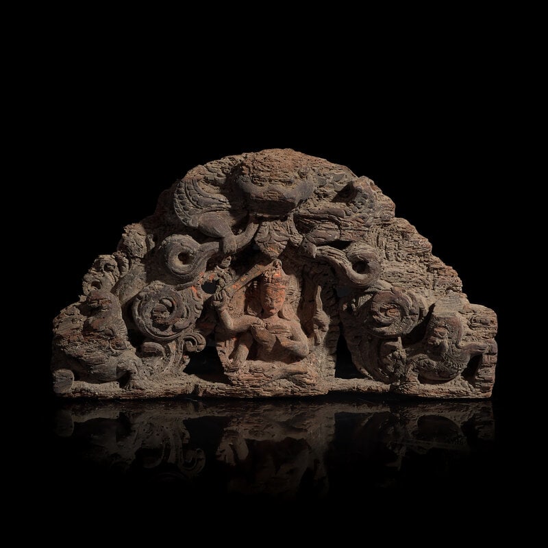 A Nepalese Carved Wood Torana Crest, 17th/18th Century or Earlier: A Nepalese Carved Wood Torana Crest, 17th/18th Century or Earlier 17th/18th Century or earlier Centered by a seated four-armed deity, possibly Manjusri, bearing a sword and a bow, flanked by