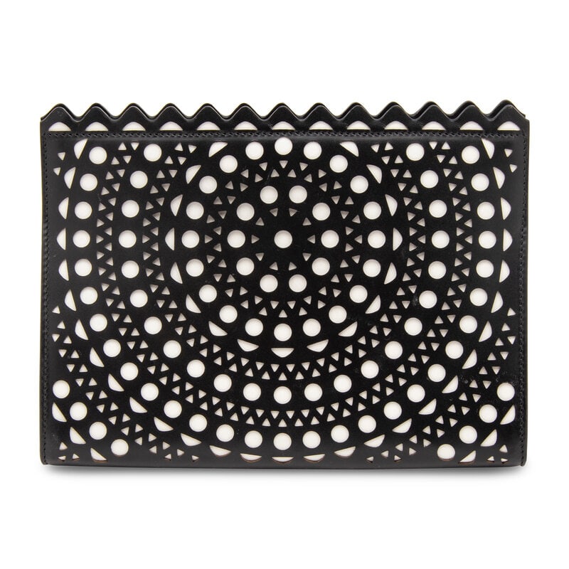 ALAÏA, LASER-CUT LEATHER CLUTCH: ALAÏA, LASER-CUT LEATHER CLUTCH Clutch in smooth black laser-cut leather with a white leather underlayer. Magnetic snap closure and wristlet strap. Label: Alaïa Style/Serial No.: