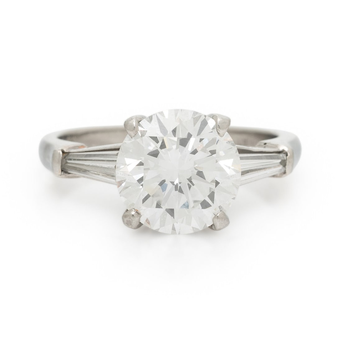 CARTIER, DIAMOND AND PLATINUM RING: CARTIER, DIAMOND AND PLATINUM RING Featuring a round diamond weighing 2.78 carats, flanked by two tapered baguette cut diamonds weighing approximately 0.25 carat total. Mounted in platinum. Ring size