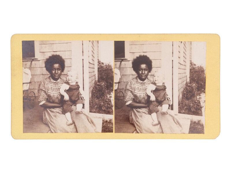 [African Americana] Stereoview of African American woman and white child seated on a front porch: [African Americana] Stereoview of African American woman and white child seated on a front porch Stereoview on cardstock mount showing a young African American woman seated on the front porch of a