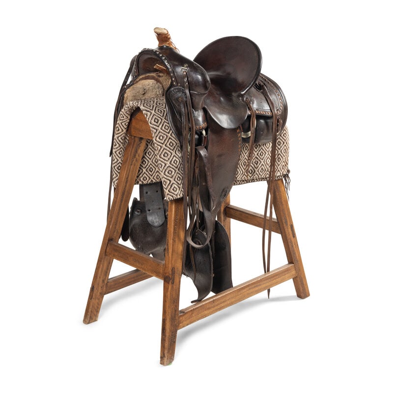 A High Backed Western Saddle, by Duhamel Co. Makers, Rapid City: A High Backed Western Saddle, by Duhamel Co. Makers, Rapid City lightly stamped design on edges and featuring tapadero stirrups; on a custom stand with saddle blanket. Saddle height 18 x length 26 x