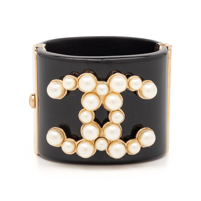 Chanel, CC Cuff Bracelet: Chanel, CC Cuff Bracelet Cuff bracelet in black composite and gold-tone metal with a faux-pearl CC embellishment. Push-lock & hinged closure. Label: Unmarked, attributed to Chanel Date: