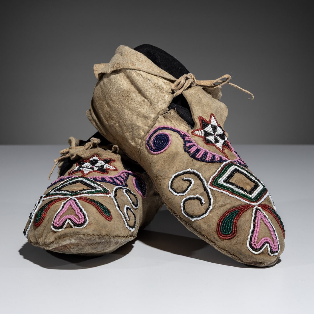 Dakota Beaded Buffalo Hide Moccasins: Dakota Beaded Buffalo Hide Moccasins fourth quarter 19th century sinew-sewn and beaded with colors of cobalt, pink, white, translucent green, and rose; designed with floral and avian elements length