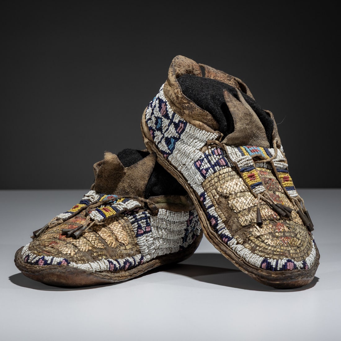 Northern Plains Beaded and Quilled Buffalo Hide Moccasins: Northern Plains Beaded and Quilled Buffalo Hide Moccasins mid-19th century sinew-sewn; plaited quillwork on vamps in faded red, yellow, and cream; beadwork in colors of white, pink, cobalt, greasy yel