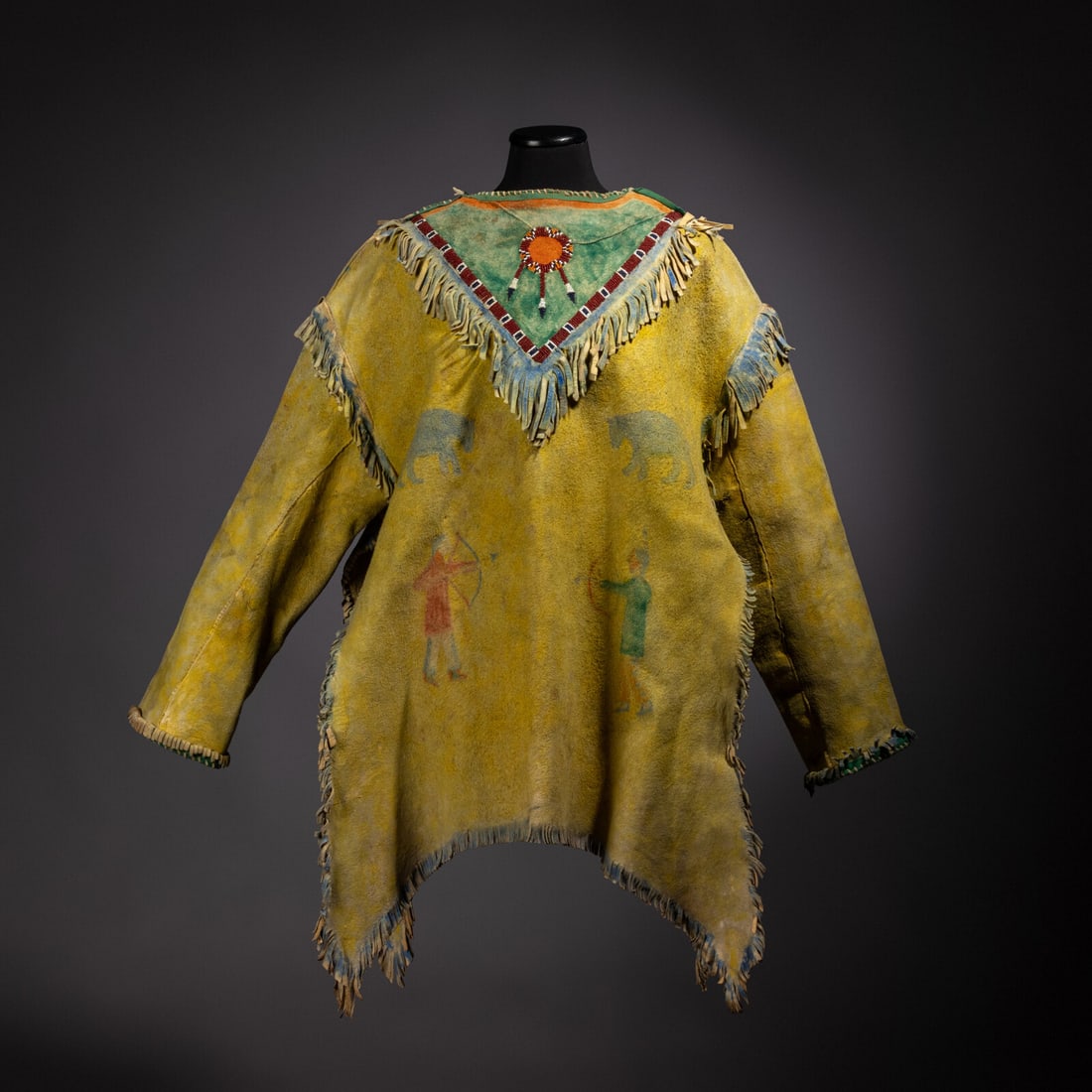 Pawnee Painted Hide Shirt: Pawnee Painted Hide Shirt first quarter 20th century thread and sinew-sewn; hide coated in yellow pigment and decorated with bears and men holding bows and arrows; fringe highlighted in blue; bib is p