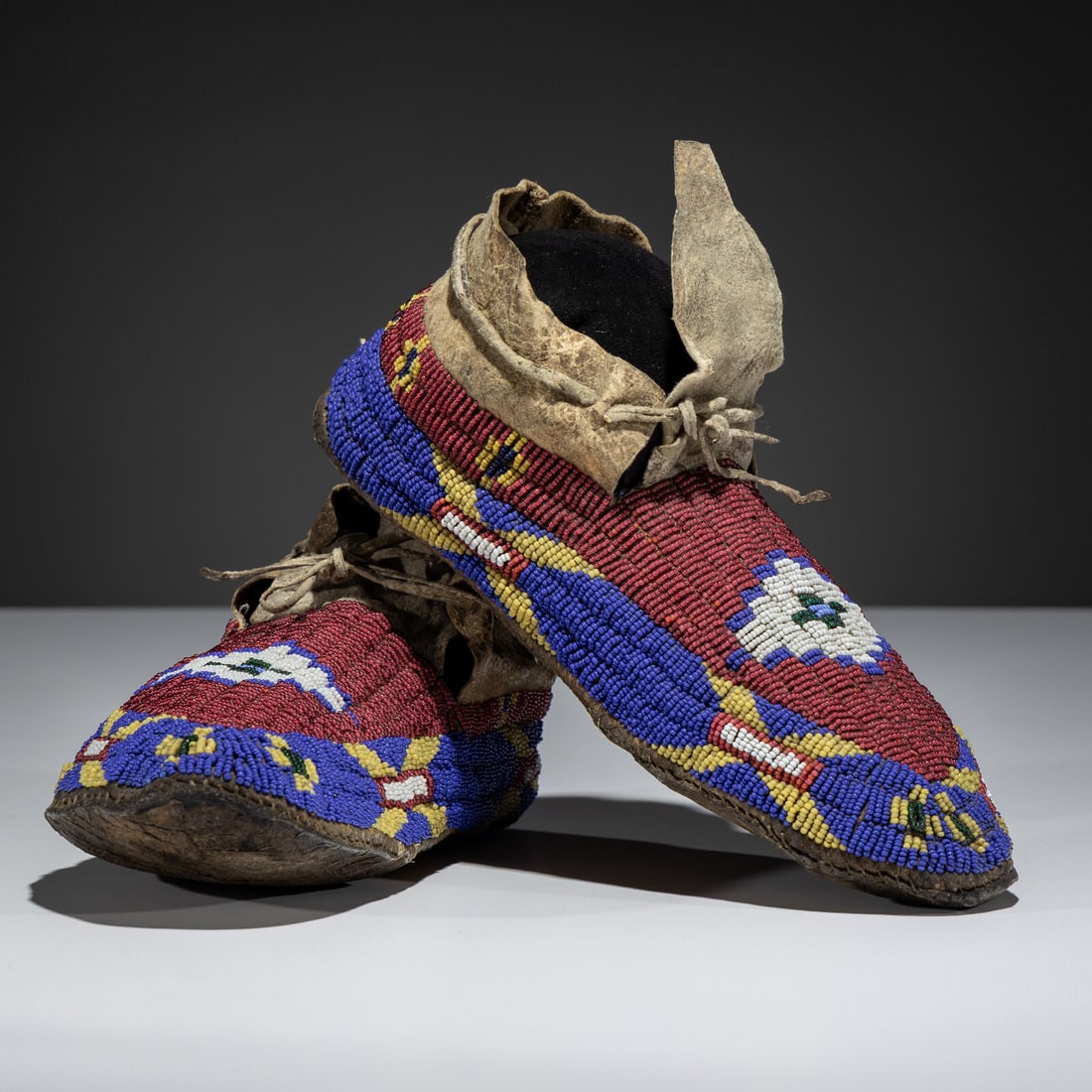 Sioux Beaded Buffalo Hide Moccasins: Sioux Beaded Buffalo Hide Moccasins fourth quarter 19th century thread and sinew-sewn; beaded using colors of red white-heart, dark blue, greasy yellow, and white; stepped diamond on vamps length 10-1