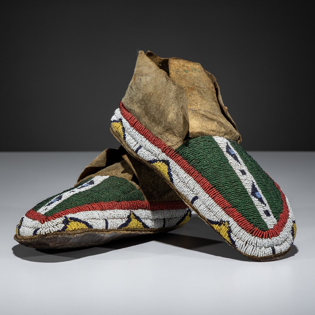 Sioux Beaded Buffalo Hide Moccasins: Sioux Beaded Buffalo Hide Moccasins fourth quarter 19th century sinew-sewn and beaded using colors of red white-heart, translucent green, cobalt, white, and greasy yellow length 10-1/2 inches
