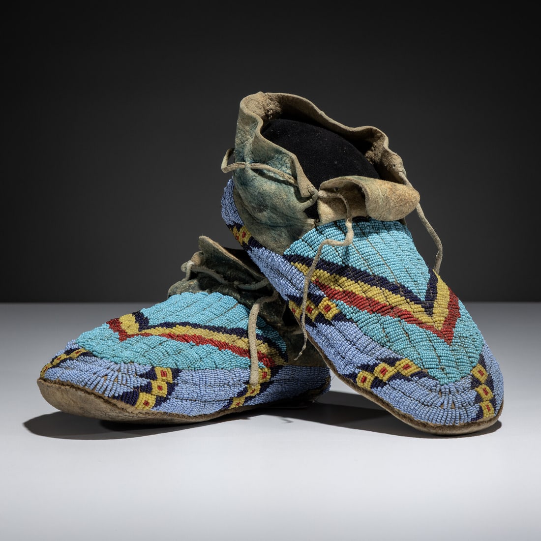 Sioux Beaded Buffalo Hide Moccasins: Sioux Beaded Buffalo Hide Moccasins fourth quarter 19th century sinew-sewn and beaded in light blue, medium blue, cobalt, red white-heart, and greasy yellow; blue pigment on hide length 10 inches Ex T