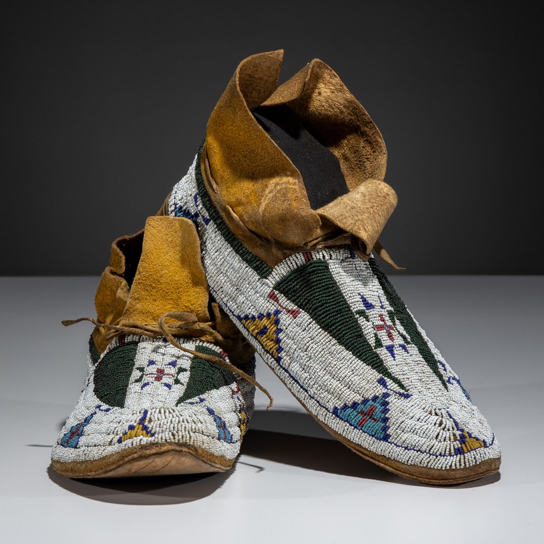 Cheyenne Beaded Hide Moccasins: Cheyenne Beaded Hide Moccasins fourth quarter 19th century sinew-sewn; beaded with geometric elements, including a central Morning Star, in colors of red white-heart, translucent green, navy blue,