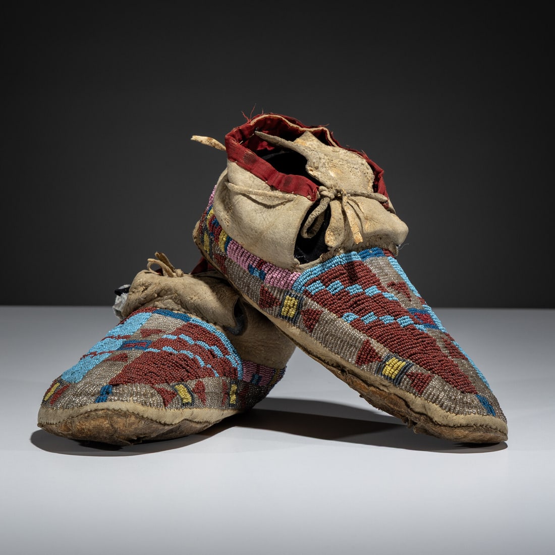 Northern Cheyenne / Arapaho Beaded Moccasins, with Recycled Buffalo Parfleche Soles: Northern Cheyenne / Arapaho Beaded Moccasins, with Recycled Buffalo Parfleche Soles fourth quarter 19th century thread and sinew-sewn, softly tanned hide; beaded in maroon, light blue, red
