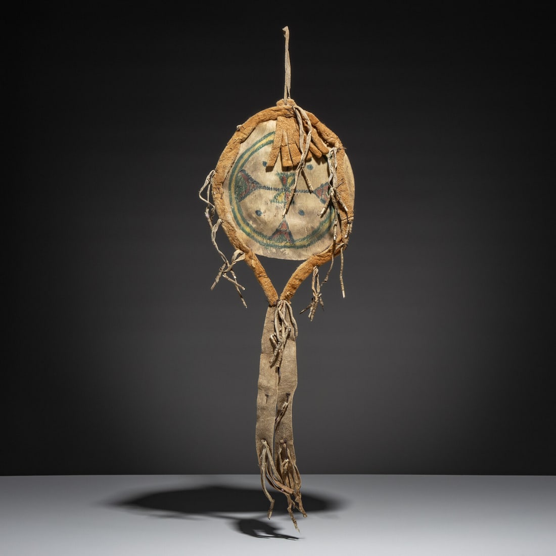 Arapaho Painted Parfleche Shield: Arapaho Painted Parfleche Shield second half 19th century diminutive size; thin parfleche disk painted in blue, green, red, and yellow is surrounded by buffalo hide diameter 7 inches; length 20