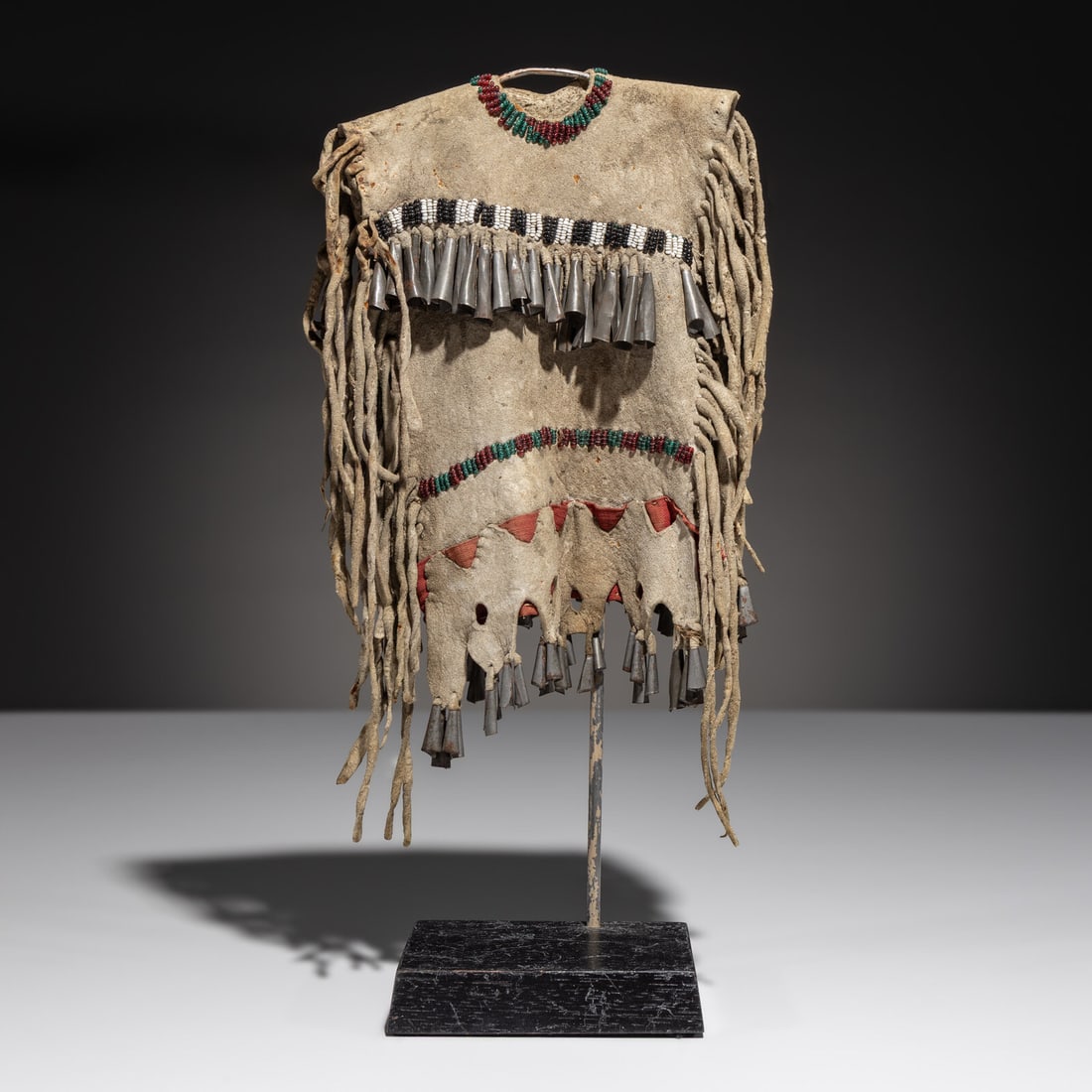 Apache Doll's Hide Dress: Apache Doll's Hide Dress late 19th century sinew-sewn, softly tanned hide; beaded with colors of rose, translucent green, white, and black; augmented with tin cone fringe and red cotton length 9 inche