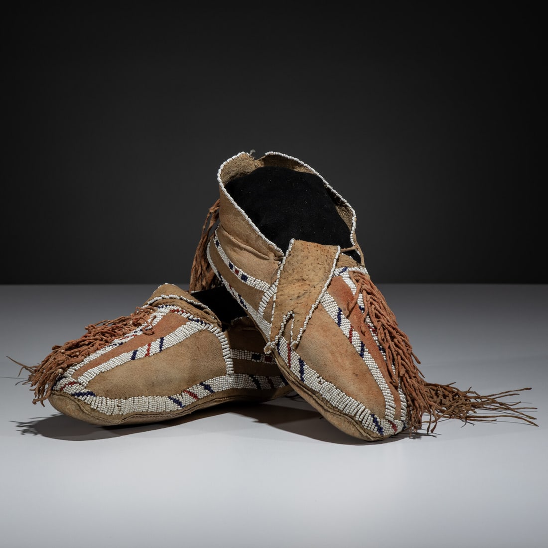 Southern Cheyenne Beaded Hide Moccasins: Southern Cheyenne Beaded Hide Moccasins fourth quarter 19th century sinew-sewn, softly-tanned hide; lanes beaded in white, cobalt, and red white-heart; forked tongues; twisted fringe dusters; red pigm