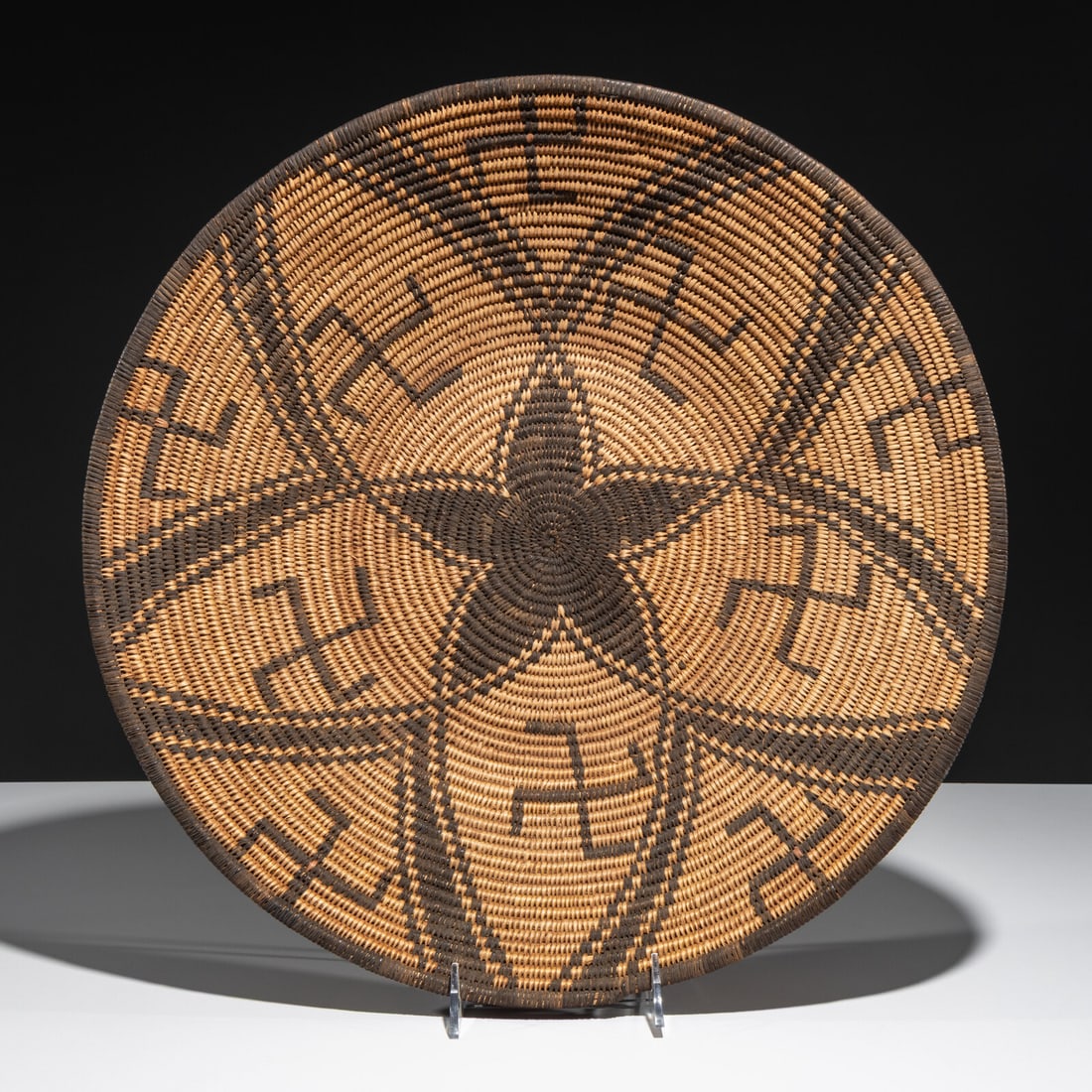 Apache Basket: Apache Basket early 20th century overall petal design with whirling logs height 3-3/4 inches x diameter 17-1/4 inches Property From a Private Virginia Collection This lot is located in Chicago.