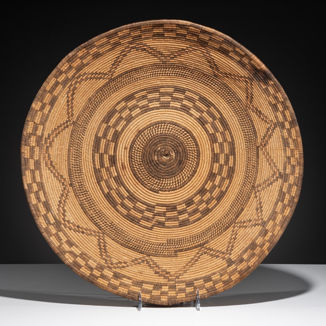 Apache Polychrome Basket: Apache Polychrome Basket early 20th century checkered bands offset with an outline zigzag; faded pink pigment height 4-1/2 inches x diameter 18 inches Property From a Private Virginia Collection 