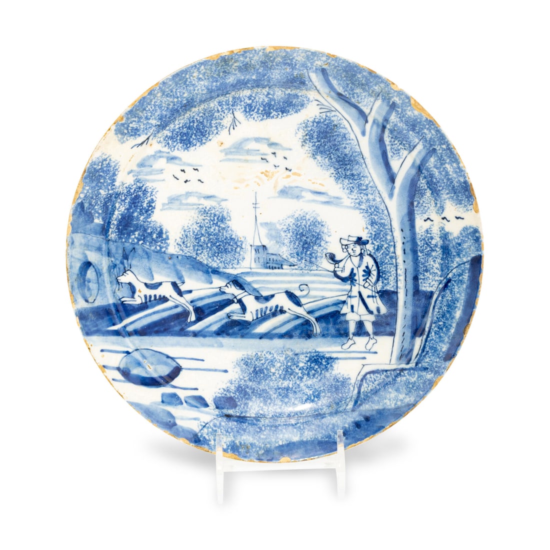 A Dutch Delft Hunt-Scene Dish: A Dutch Delft Hunt-Scene Dish First Half 18th Century decorated in blue-and-white and showing a hunter with horn and two hounds within a landscape. Diameter 9 inches. Property from the East Coast