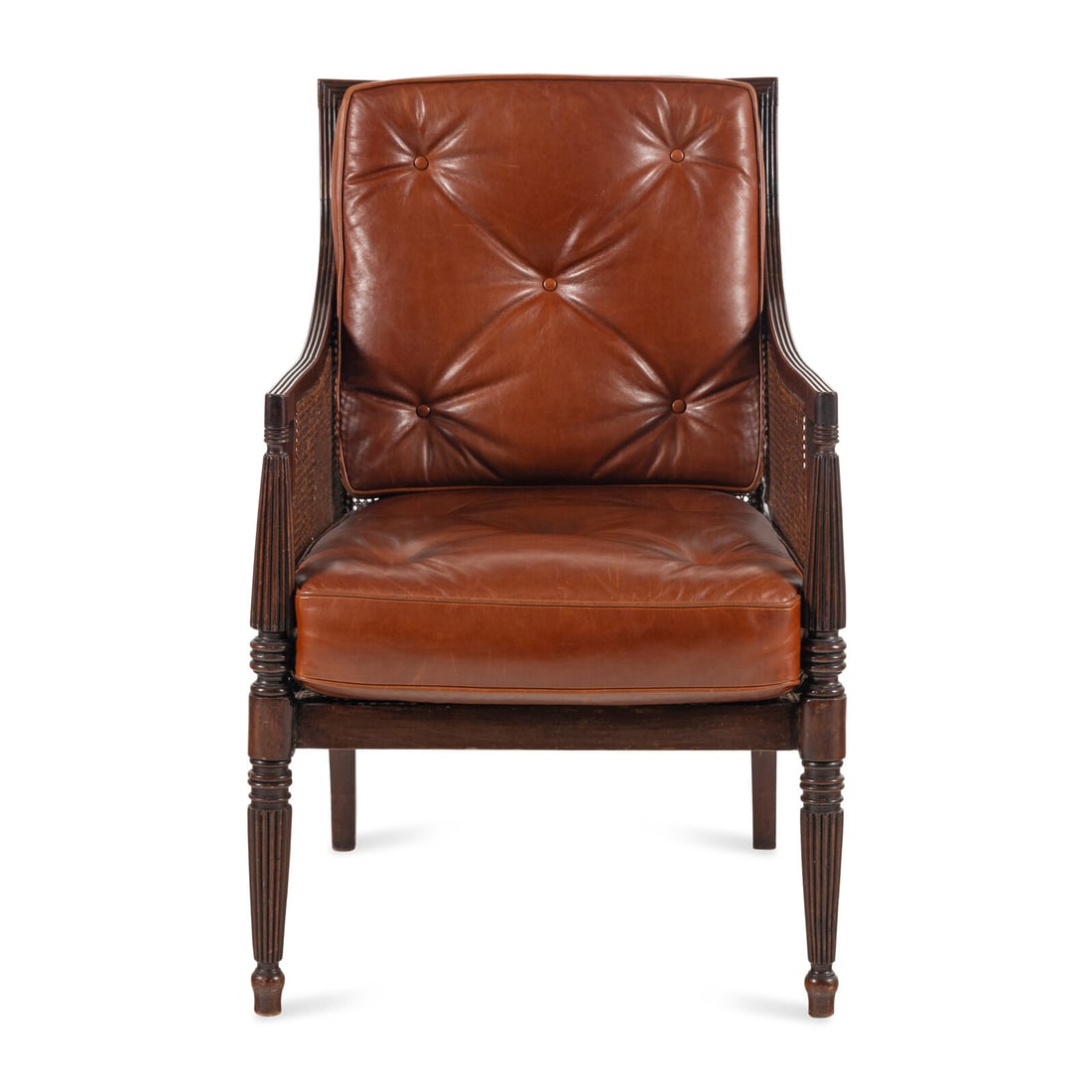 An English Mahogany and Caned Library Bergère: An English Mahogany and Caned Library Bergère 19th Century having reeded frame with a caned back, seat and sides with two foam-stuffed leather cushions. Height 36 x width 24 x depth 25 inches.