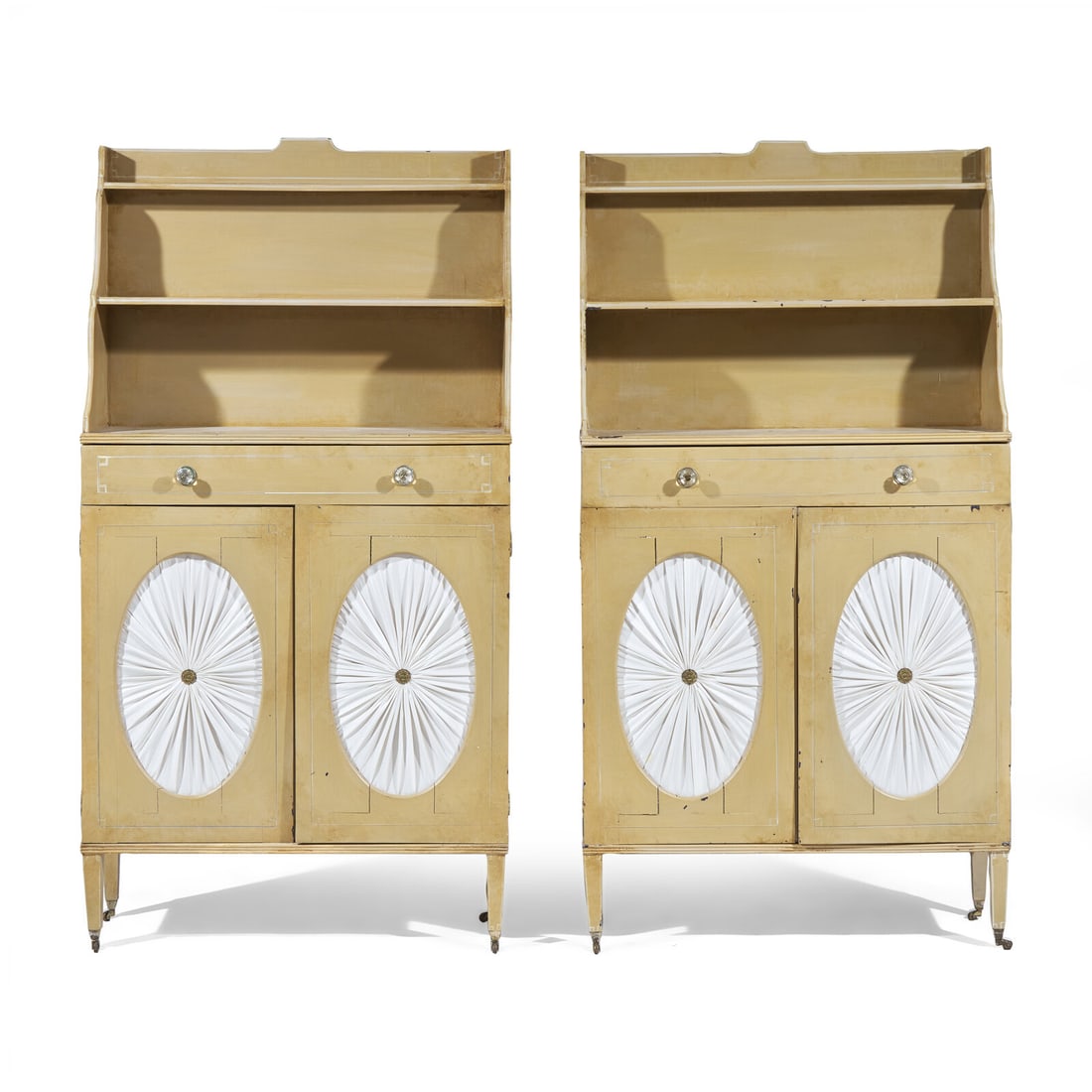 A Pair of Regency Style Painted Chiffonieres: A Pair of Regency Style Painted Chiffonieres 20th Century each with single drawer over two doors with cut oval roundels revealing ruched white silk, the interior with removable shelf, on tapered squar