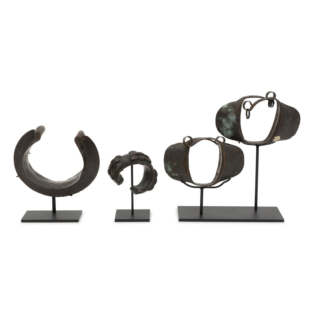 Four African Bronze Adornments on Fitted Stands: Four African Bronze Adornments on Fitted Stands 19th Century comprising one collar, one bangle with molded cowrie shell decoration, and a pair of rattling anklets. Anklet, width 7 1/4 inches; Bangle, 