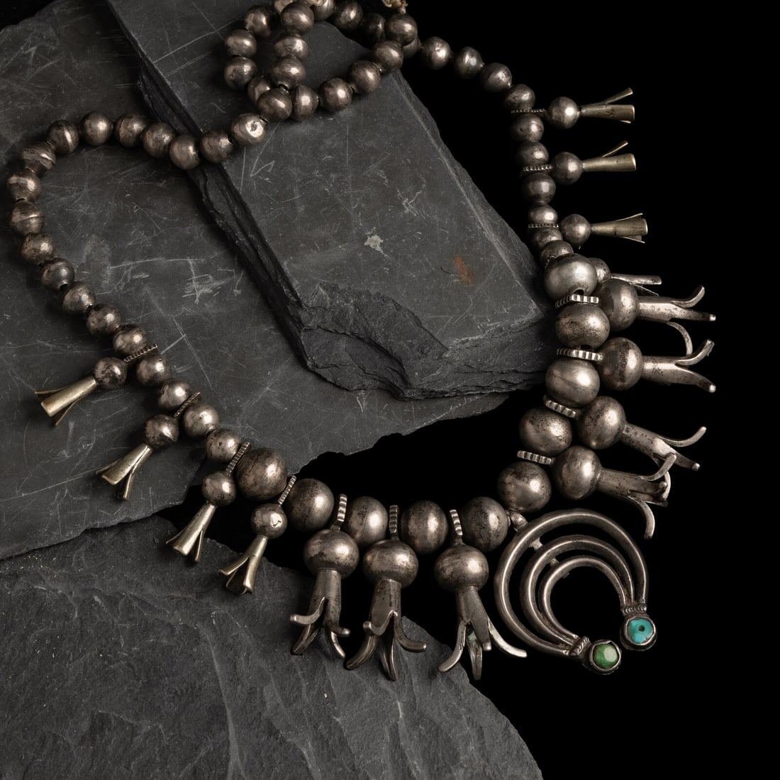 Early Navajo Ingot and Turquoise Squash Blossom Necklace: Early Navajo Ingot and Turquoise Squash Blossom Necklace ca 1900 fifteen squash blossoms, each with chiseled elements on the bail; the naja triple-crescent naja terminates with two turquoise stones, o