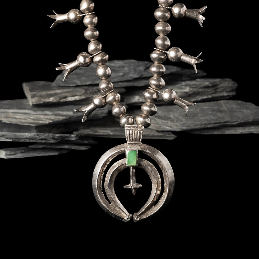 Navajo Squash Blossom Necklace: Navajo Squash Blossom Necklace first quarter 20th century single strand necklace strung with twelve blossoms, and featuring a central double crescent naja, set with a single turquoise stone; not
