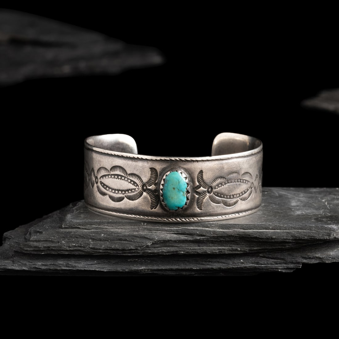 Navajo Ingot and Turquoise Cuff Bracelet: Navajo Ingot and Turquoise Cuff Bracelet early 20th century stamped shank with central stone set in a serrated bezel with chiseled bands on the edge; not marked width 7/8 inch interior circumference 5