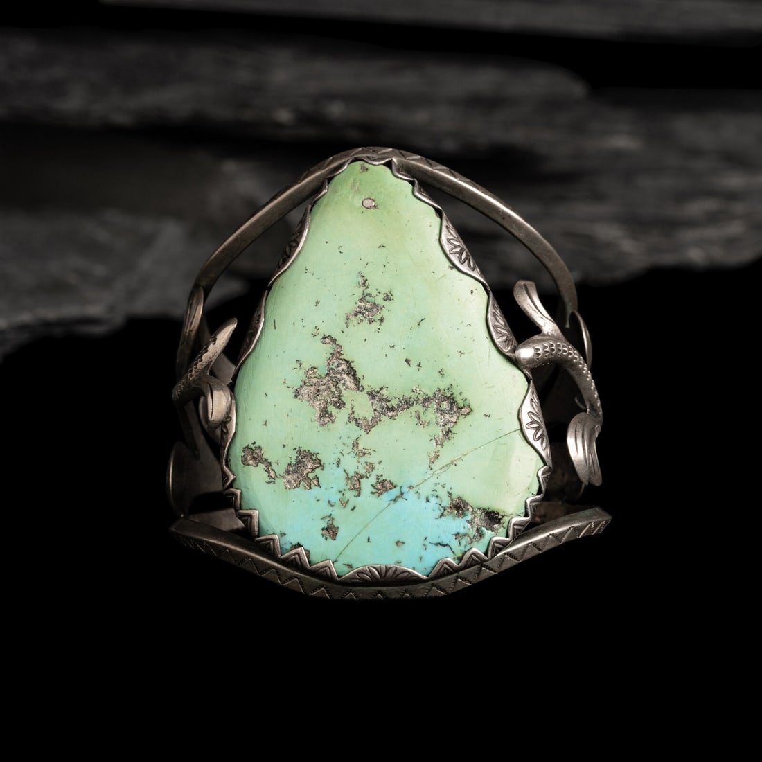 Navajo Silver and Turquoise Cuff Bracelet: Navajo Silver and Turquoise Cuff Bracelet second quarter 20th century stamped carinated bands housing sandcast scrolling leaf elements set with a large single stone in a stamped serrated bezel; not ma