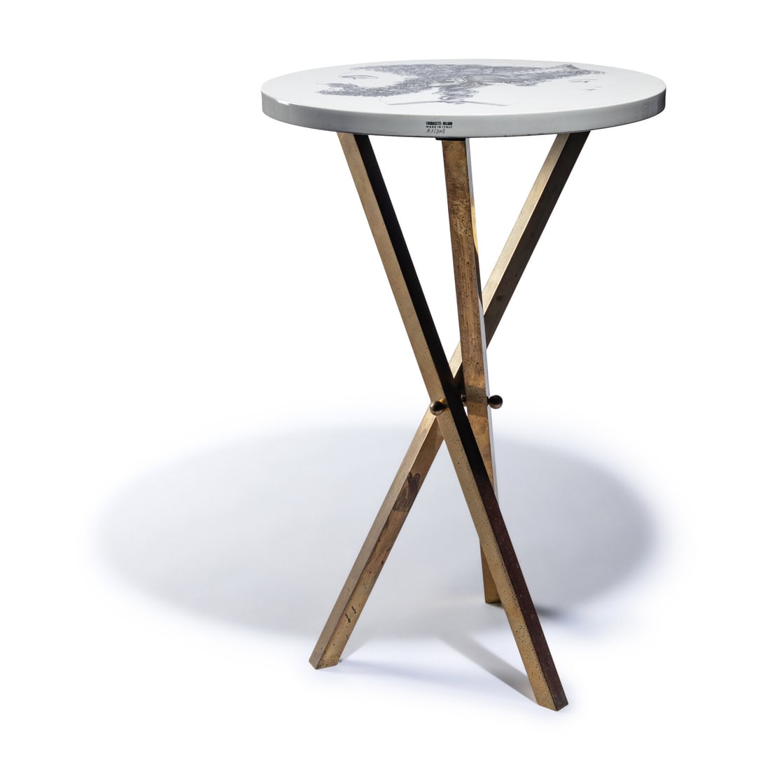 Piero Fornasetti (Italian, 1913-1988) 'Giano Bifronte' Side Table: Piero Fornasetti (Italian, 1913-1988) 'Giano Bifronte' Side Table lithographic transfer-print over wood, brass stamped to rim 'Fornasetti ? Milano Made in Italy, N. N. 2003' 22 h x 14 dia inches. This