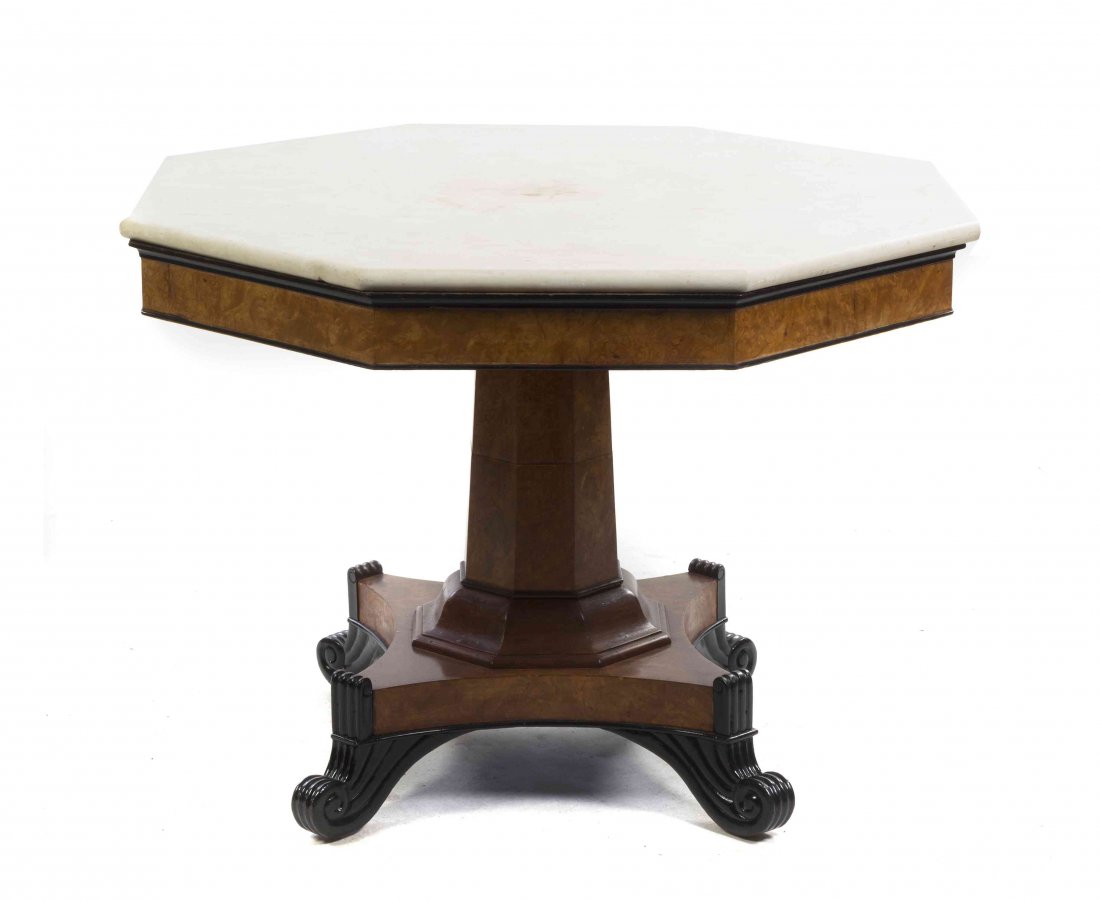 A Biedermeier Burlwood and Parcel Ebonized Center: A Biedermeier Burlwood and Parcel Ebonized Center Table, having an octagonal marble top over the plain frieze, raised on a faceted tapering standard, set on a quadripartite base ending in scrolled fee