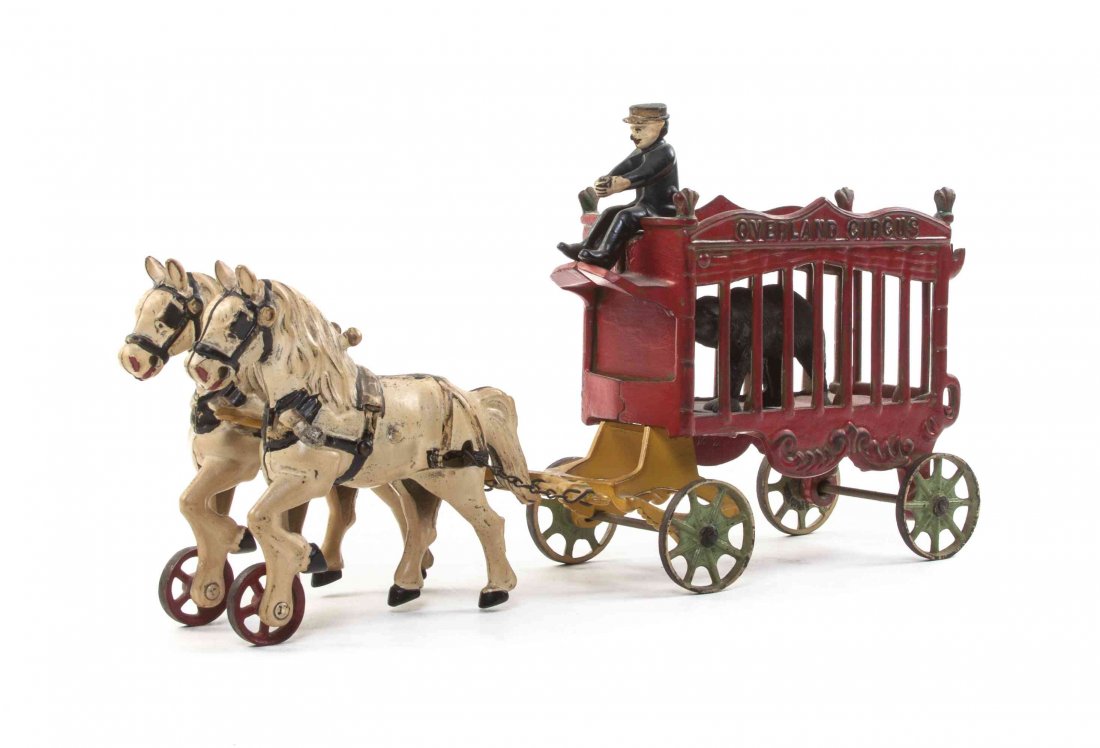 An American Cast Iron Overland Circus Wagon, Length: An American Cast Iron Overland Circus Wagon, with a team of two horses and a single driver pulling a cart holding a caged bear. Length overall 13 inches.