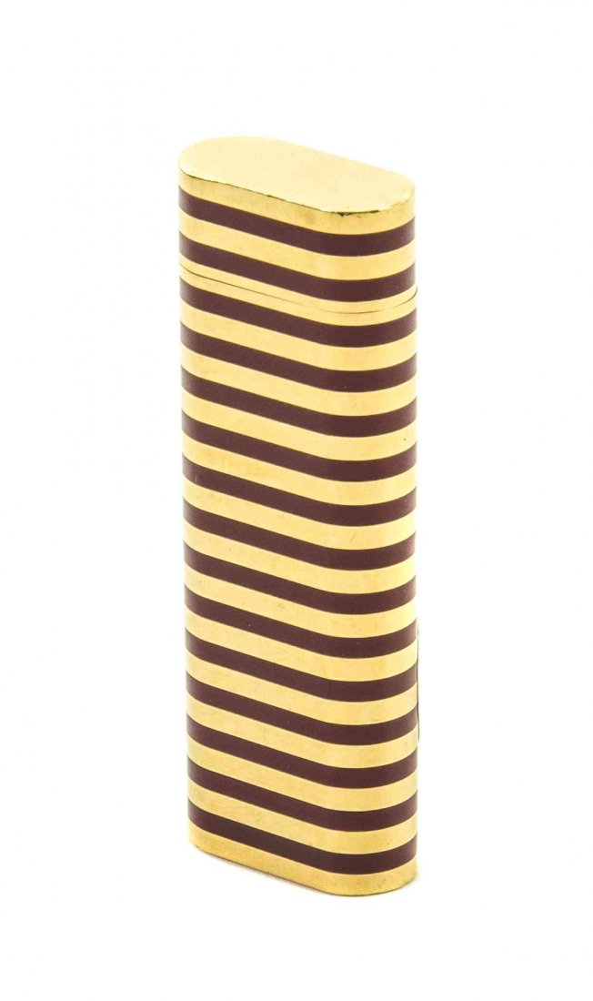 A Swiss Enameled Gilt Metal Lighter, retailed by: A Swiss Enameled Gilt Metal Lighter, retailed by Cartier, Paris, of flattened cylindrical form with linear decoration, having a butane lighting mechanism, set in a fitted red leather Cartier box. Heig