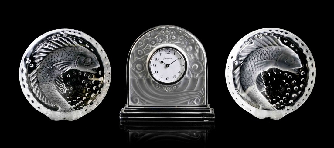 Three Glass Table Articles, Height of clock 6 3/8: Three Glass Table Articles, comprising a Baccarat mantel clock, and a pair of Lalique fish ash receivers. Height of clock 6 3/8 inches. Property from a Private Collection, Palm Beach, Florida