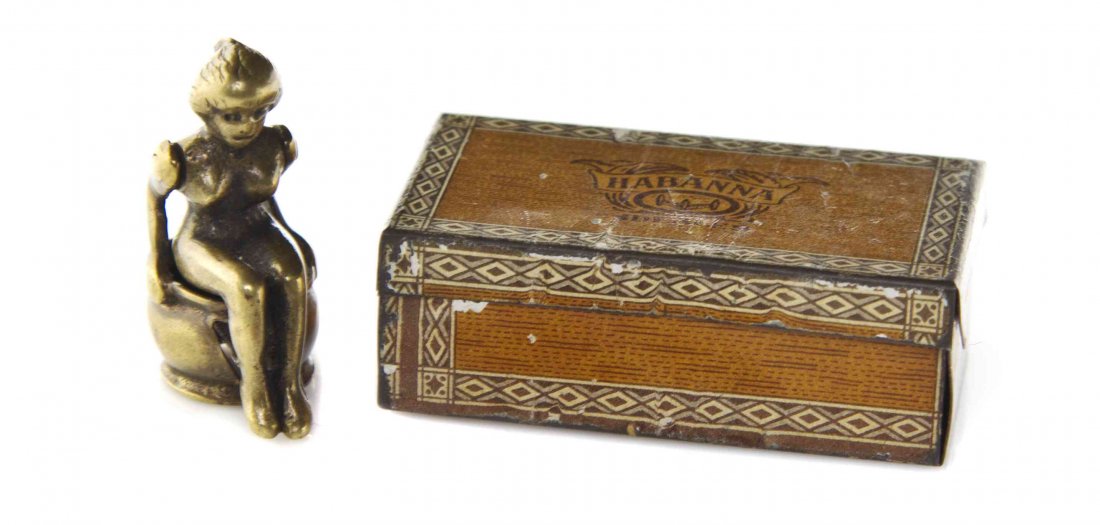 A Whimsical Brass Cigar Cutter, Height of first 1 3/8: A Whimsical Brass Cigar Cutter, in the form of a nude maiden using a chamber pot, together with a tin Habanna cigar box containing three cigars. Height of first 1 3/8 inches. The Adell Venus Collectio