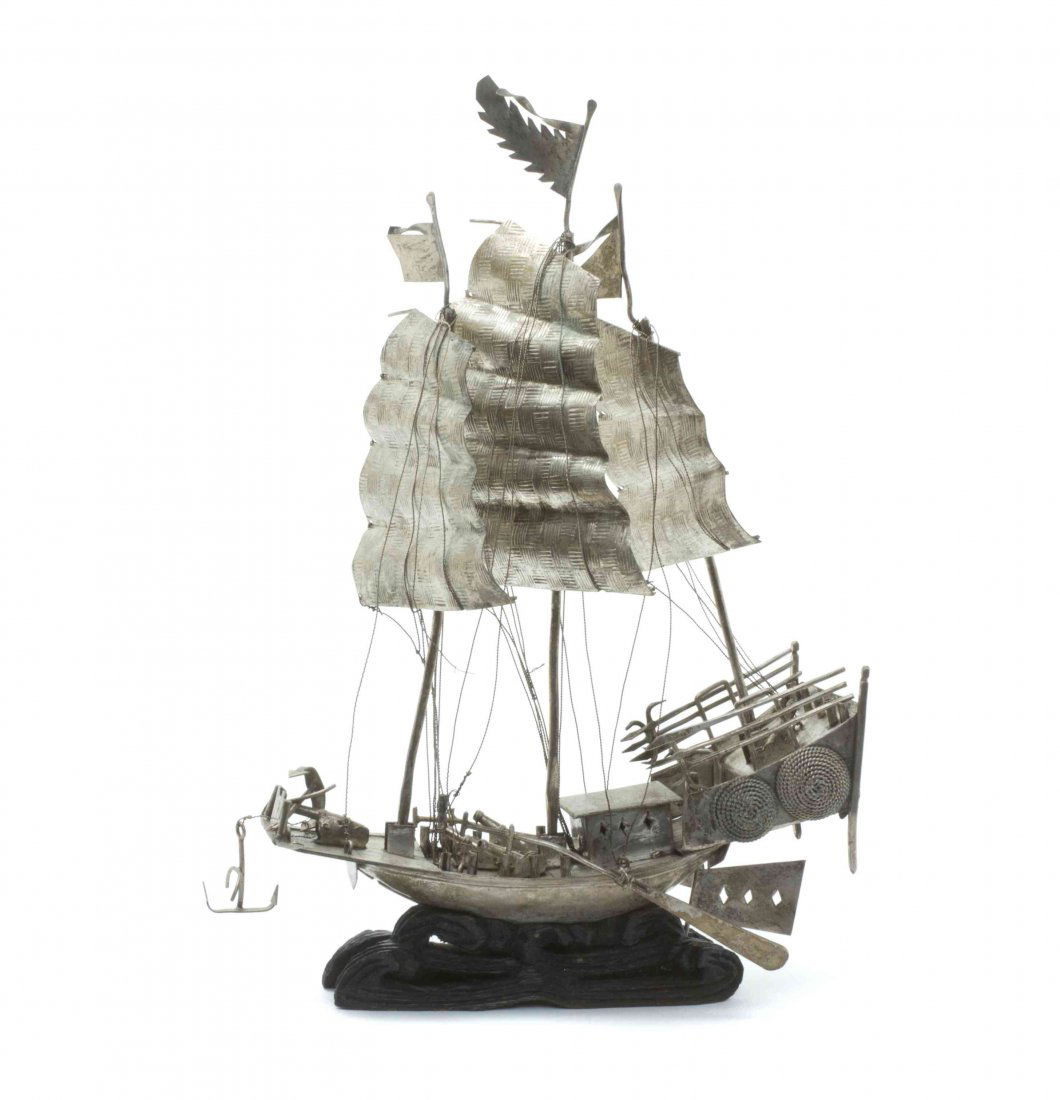 A Chinese Silvered Metal Model of a Junk, Height 10 1/4: A Chinese Silvered Metal Model of a Junk, the vessel depicted with three masts and sails surmounted with flags, having articulated elements and riggings, raised on a hardwood base carved to depict rol