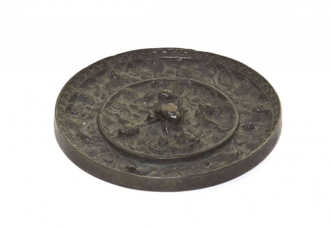 A Chinese Bronze Mirror, Diameter 4 1/4 inches.: A Chinese Bronze Mirror, having central lion form cord loop surrounded by striding beasts in the interior border with foliate and clusters of grapes, the exterior border having decoration of birds, ri