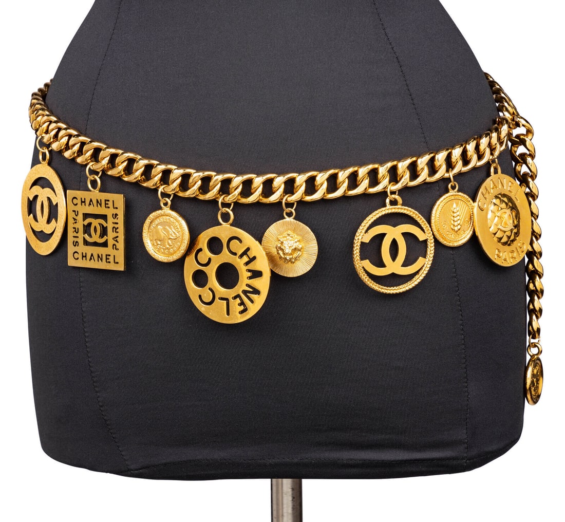 Chanel, Oversized Charm Chain Belt: Chanel, Oversized Charm Chain Belt Chain belt in gold-tone metal with oversized logo & medallion charms. Hook closure and dangling medallion coin. Label: Chanel Date: Late 1980's - Early 1990's Countr