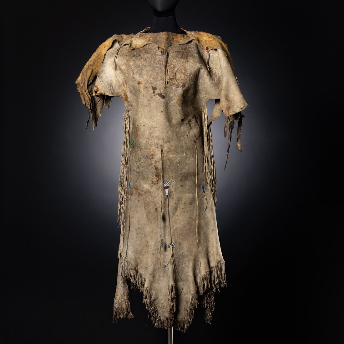 Early Upper Missouri Hide Dress: Early Upper Missouri Hide Dress second quarter 19th century classic, two-skin style dress; sinew-sewn with fringe along side seams; beaded triangular tabs in colors of white, red white-heart, pony tra