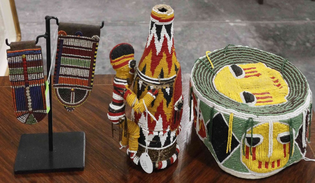 Three Yoruba Beaded Articles, Height of bottle 9 1/4: Three Yoruba Beaded Articles, comprising a hat with fringe at the top, a bottle with an applied figure and a pair of ear clips raised on a metal stand. Height of bottle 9 1/4 inches. Property from the