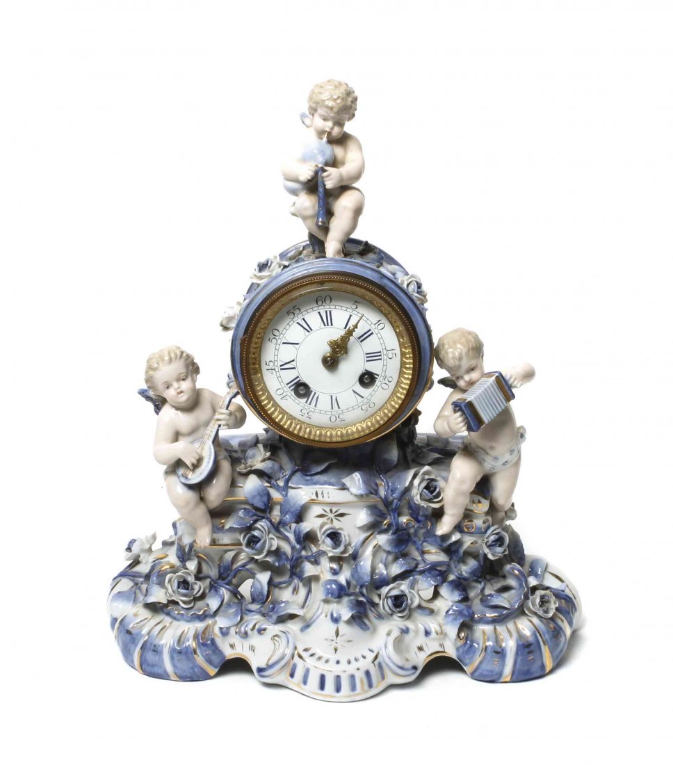 A German Porcelain Mantel Clock, Height 14 1/2 x width: A German Porcelain Mantel Clock, having a circular dial within a musical cherub mounted and Rococo worked case. Height 14 1/2 x width 12 x depth 4 1/2 inches.