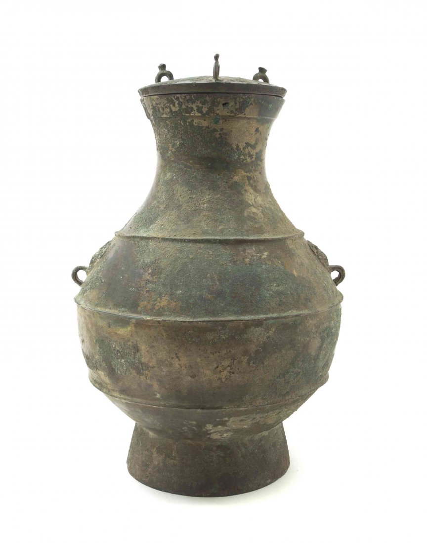 A Chinese Gilt Bronze Covered Hu-Form Vessel, Height ov: A Chinese Gilt Bronze Covered Hu-Form Vessel, Han Dynasty, the lid surmounted with three upright loops, having archaic bird masks, their hooked beaks forming small loop handles, raised on a pedestal f