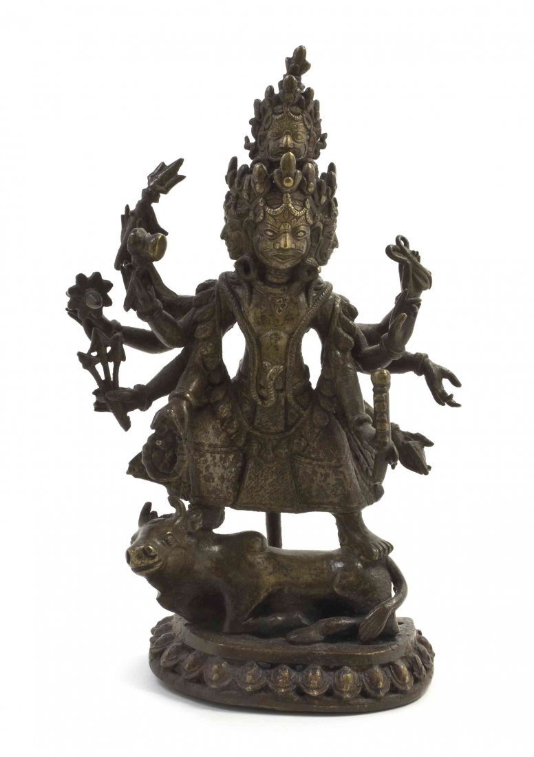 A Tibetan Bronze Multi-Armed Deity, Height overall 9: A Tibetan Bronze Multi-Armed Deity, the figure depicted standing upon a recumbent ox, having multiple faces and arms and bearing various attributes, raised on a lotus base. Height overall 9 1/4 inches