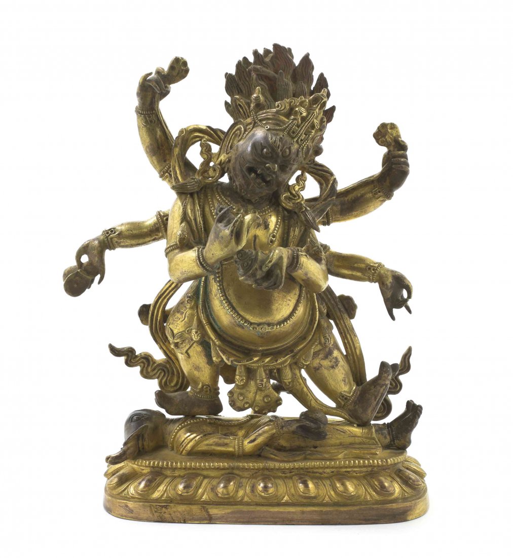 A Tibetan Gilt Bronze Multi-Armed Figure, Height 9 3/4: A Tibetan Gilt Bronze Multi-Armed Figure, the deity depicted holding multiple attributes and standing upon a recumbent figure, raised on a lotus base. Height 9 3/4 inches.