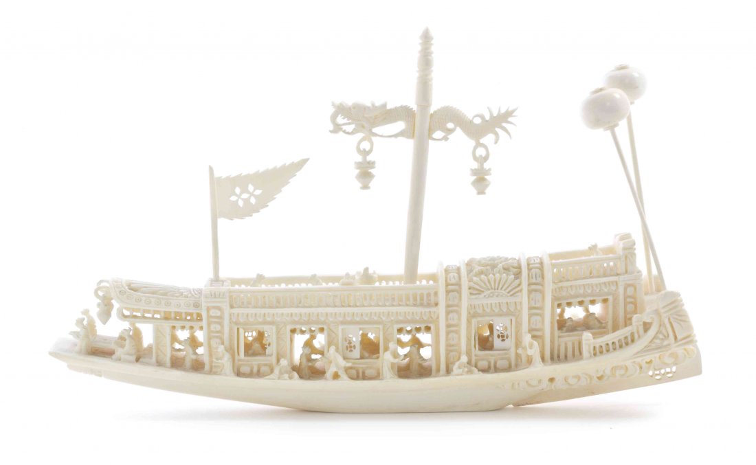 A Chinese Carved Ivory Boat, Width 8 3/4 inches.: A Chinese Carved Ivory Boat, the vessel outfitted with a dragon post and flag, having detailed architectural elements including pendent lamps, bearing passengers at various pursuits. Width 8 3/4 inche