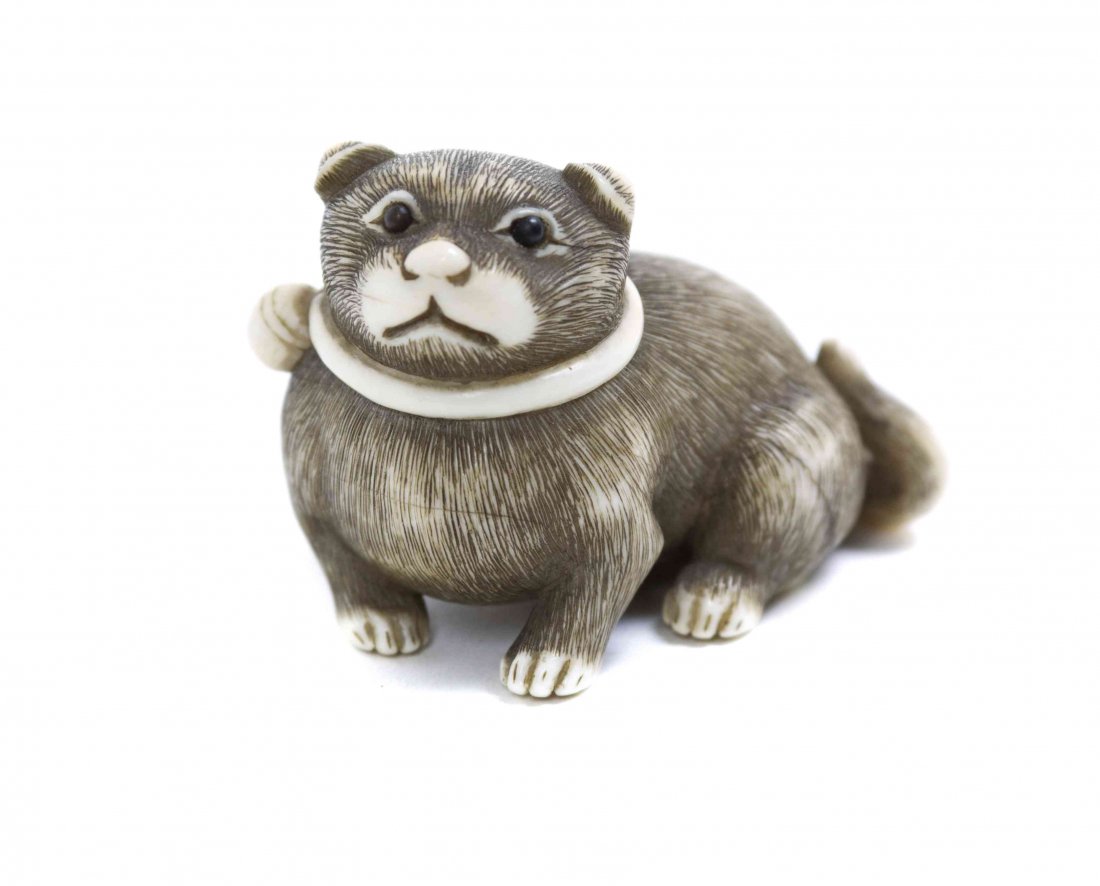 A Carved Ivory Puppy Netsuke, Width at widest 2 inches.: A Carved Ivory Puppy Netsuke, having finely incised fur, depicted recumbent and wearing a collar with a bell, signed Masatomo. Width at widest 2 inches. Property from the Collection of Dr. J. Don Nels