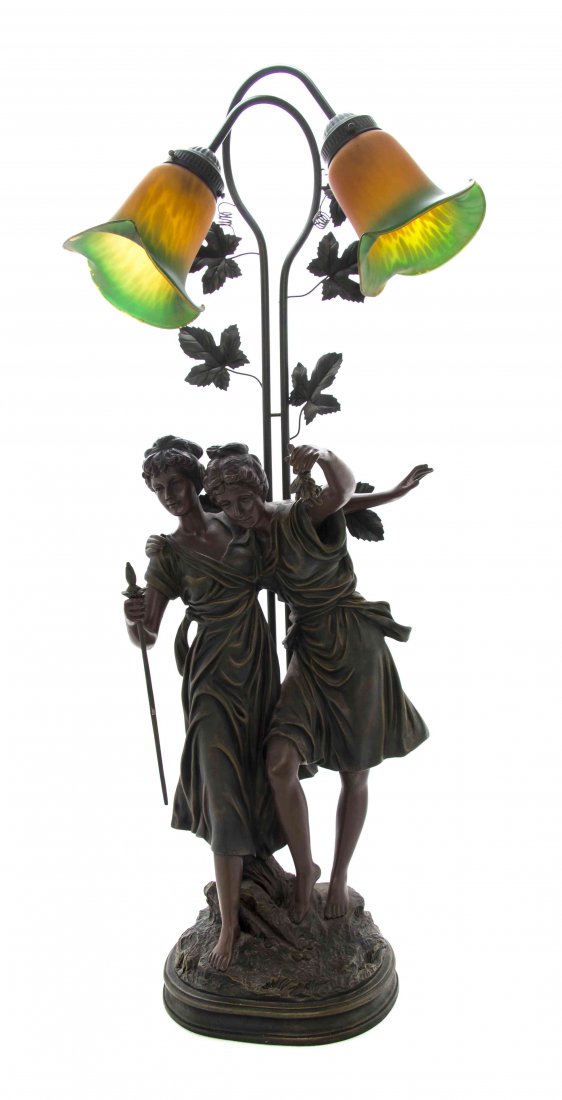 An Art Nouveau Carved Wood Newel Post Lamp, Height: An Art Nouveau Carved Wood Newel Post Lamp, in the form of two maidens frolicking, raised on a circular naturalistic base, set with two bell form glass shades with ivy leaf decoration throughout. Heig