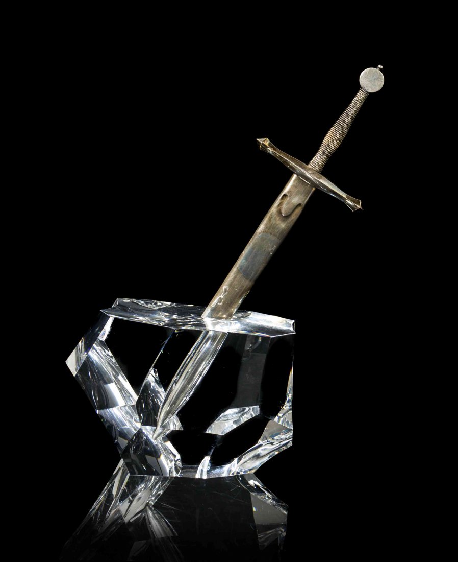 A Steuben Glass, Sterling Silver and 18 Karat Yellow: A Steuben Glass, Sterling Silver and 18 Karat Yellow Gold Paperweight, Excalibur, designed by James Houston, model 1000, introduced in 1963, modeled as King Arthur's sword embedded in a rock. Height 8